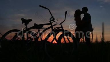 在红灰相间的夕阳下，这对相爱的夫妇在田野里温柔地接吻。 骑自行车走路